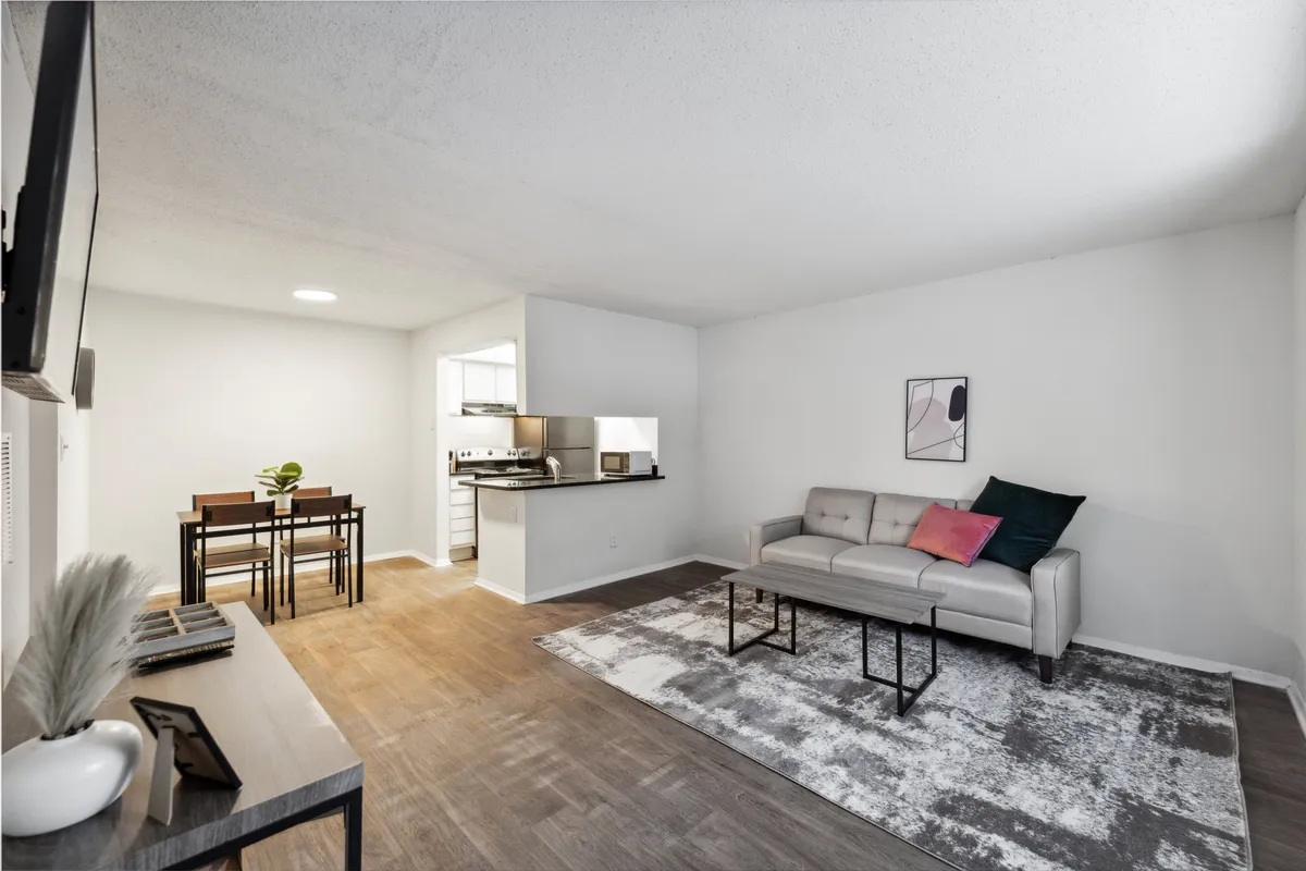 A spacious, open-concept living and dining area with a plush sofa, stylish dining table, modern kitchen area, vibrant wall art, and a cozy rug. The overall ambiance is contemporary and welcoming, filled with comfortable furnishings and tasteful décor.