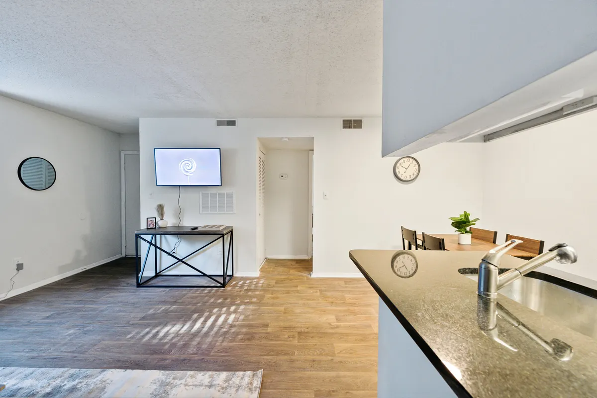 A bright, welcoming living area featuring a comfortable sofa, dining table, wall-mounted TV, and decorative mirror. The space feels inviting and home-like, perfect for relaxation or entertaining guests.