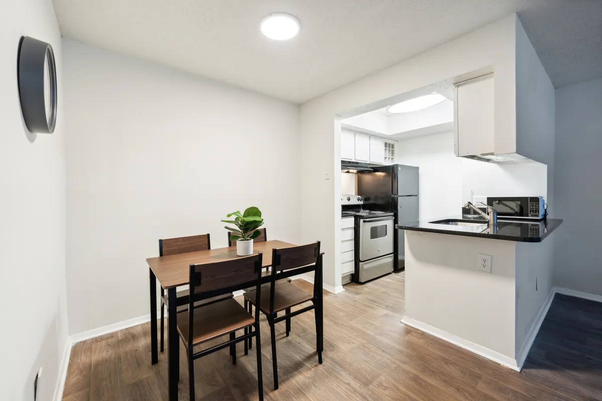 A welcoming dining table sits at the heart of a cozy kitchen area, adorned with a vibrant plant centerpiece. The setup is ideal for casual meals or intimate gatherings, with natural light streaming in and functional amenities within reach.