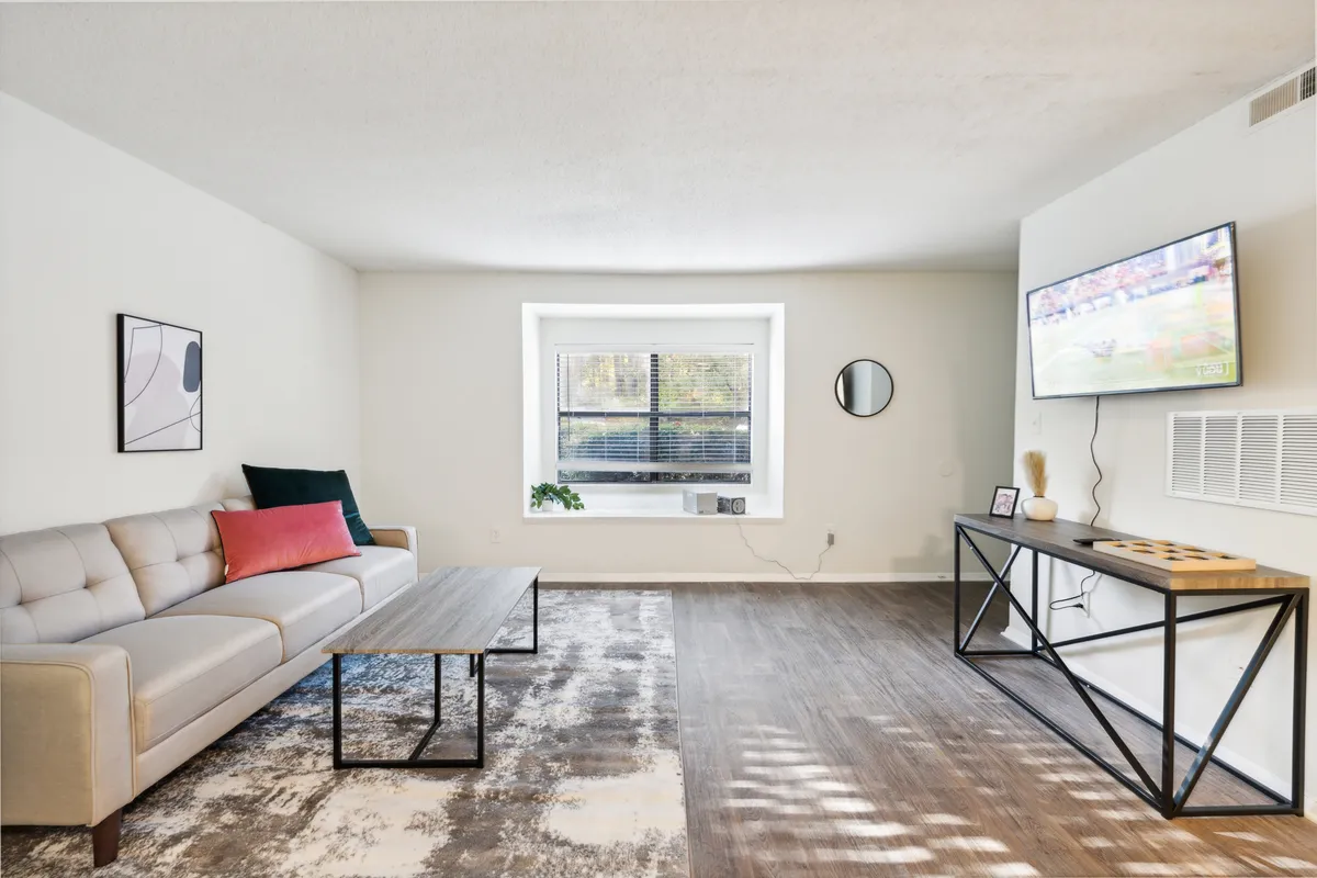 A bright living area with a comfortable sofa arranged around a coffee table, a TV mounted on the wall, decorative artwork, and a window letting in natural light. The space feels open and inviting, offering a place to relax or socialize after a day of work or exploring the city.