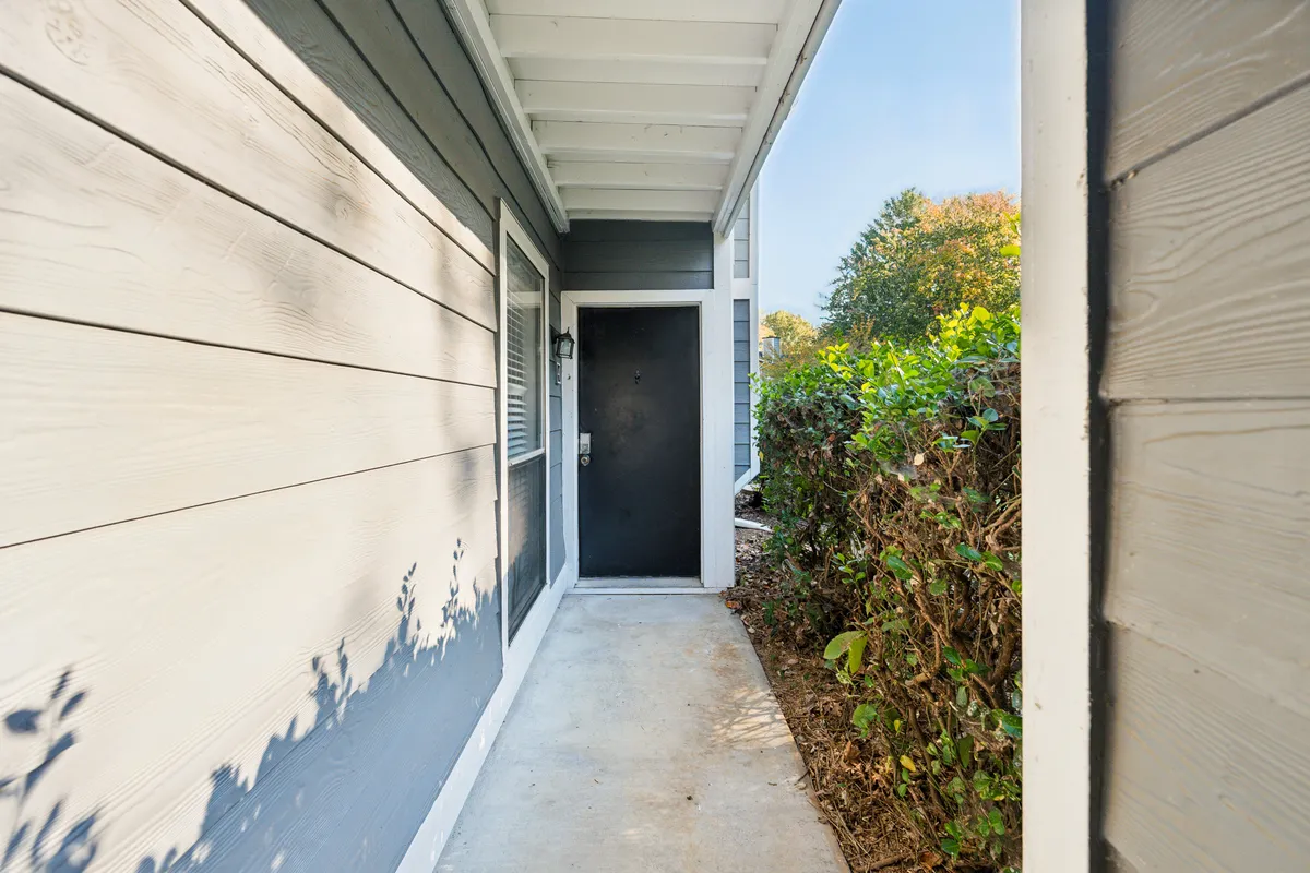 A view of the apartment’s entryway, with the front door, sidewalk, and surrounding greenery. The scene conveys a warm, inviting first impression, suggesting the ease of arrival and the welcoming atmosphere inside.