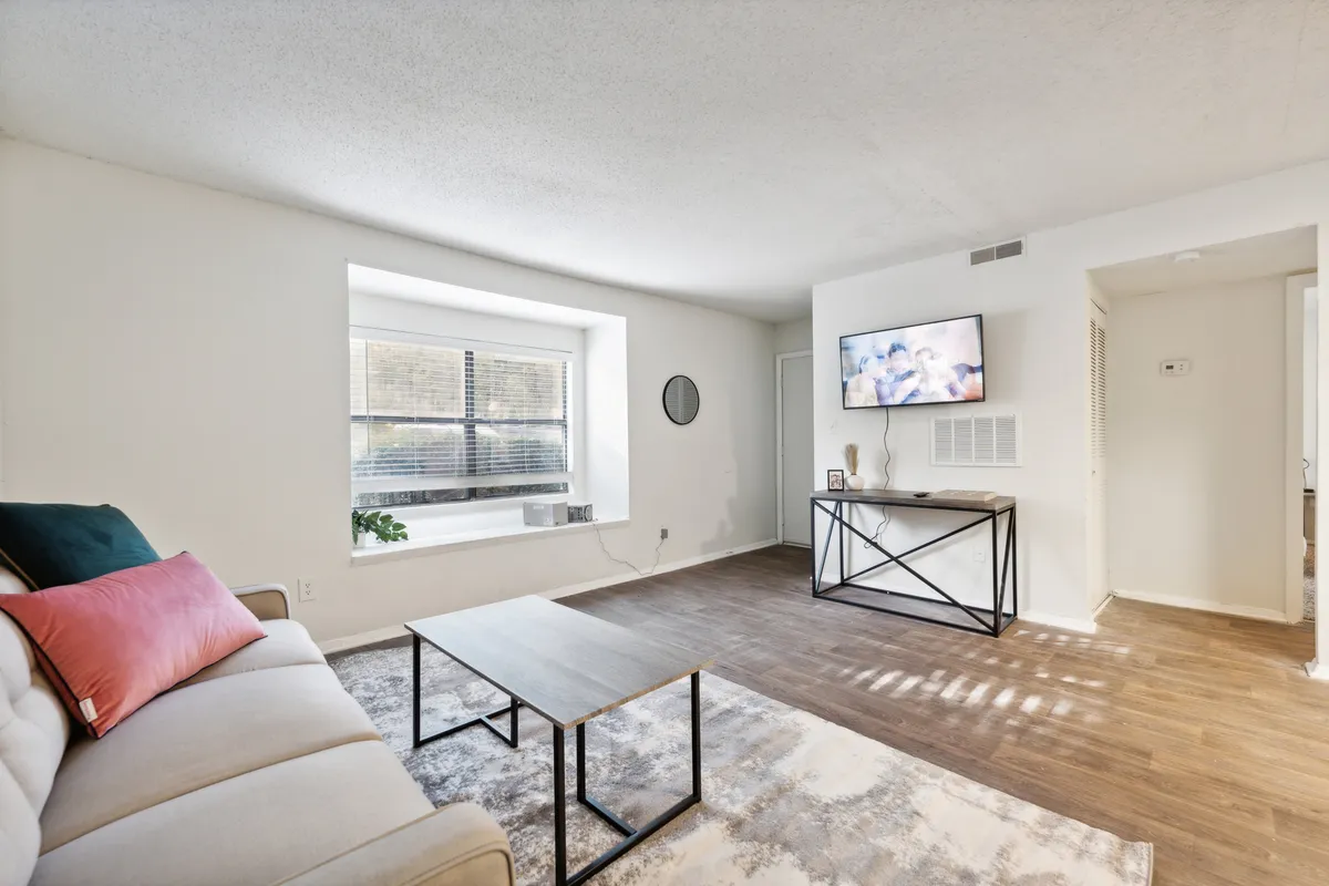 This inviting living room scene features a sofa with cushions, coffee table, TV, and a window adorned with plants. Natural light streams in, suggesting a pleasant, city-facing outlook and a connection to the bustling neighborhood beyond.